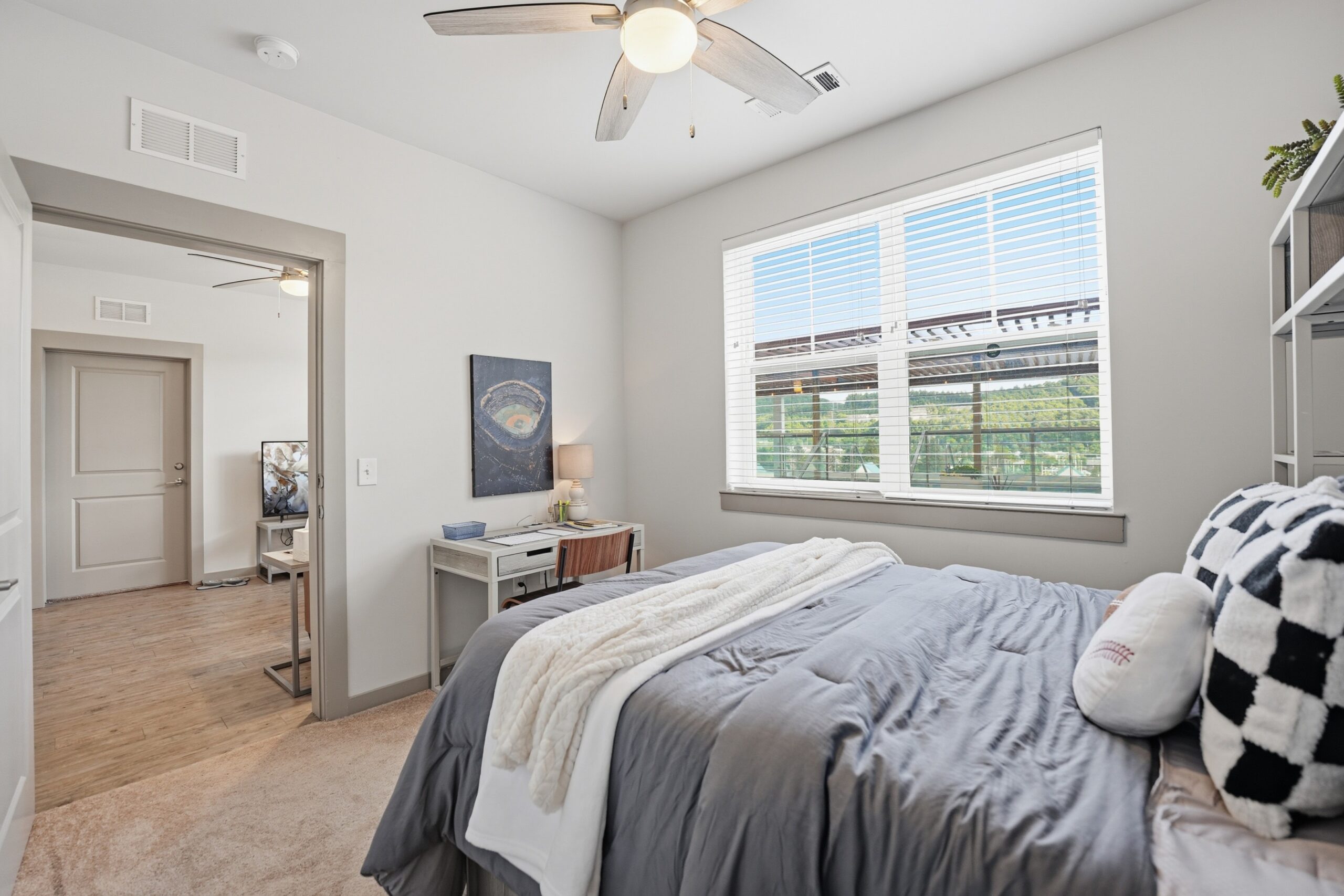 Furnished model bedroom with a ceiling fan desk and plush carpeting scaled